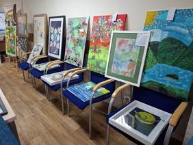 Przestronna sala. Wzdłuż ścian rozmieszczono wiele obrazów na sztalugach, krzesłach.