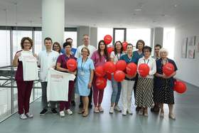 Grupa pracowników pozuje w korytarzu placówki medycznej, trzymając czerwone balony oraz koszulkę związaną z akcją