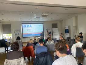 Pokaż zdjęcie: Zdjęcie przedstawia prelegenta przemawiającego podczas konferencji REHA FOR THE BLIND IN POLAND 2024 w Białymstoku. Uczestnicy siedzą na krzesłach w sali konferencyjnej, a na ekranie wyświetlany jest tytuł wydarzenia. W tle widoczne są bannery informacyjne.