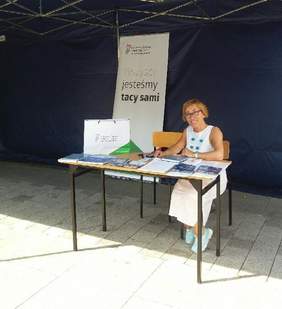 Pokaż zdjęcie: Dyrektor Oddziału Mazowieckiego siedząca przy stoliku, na którym znajdują się materiały informacyjne – Radom.