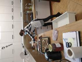 Pokaż zdjęcie: W pięknej, nowoczesnej kuchni krząta się pani. Jedna z szuflad jest otwarta. A na blacie kuchennym leżą blachy z piernikami w kształcie ścian domów i reniferów