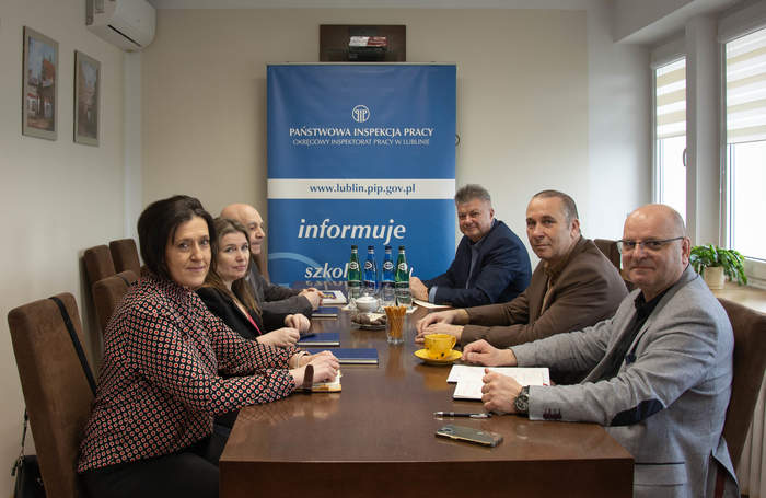 Pokaż zdjęcie: W gabinecie przy długim stole siedzą dwie kobiety oraz czterech mężczyzn, rozmawiają.