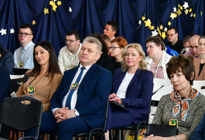 Pokaż zdjęcie: Zdjęcie osób siedzących w pierwszych rzędach podczas festiwalu. Zbliżenie na kobietę i mężczyznę ubranych w ciemne garnitury.