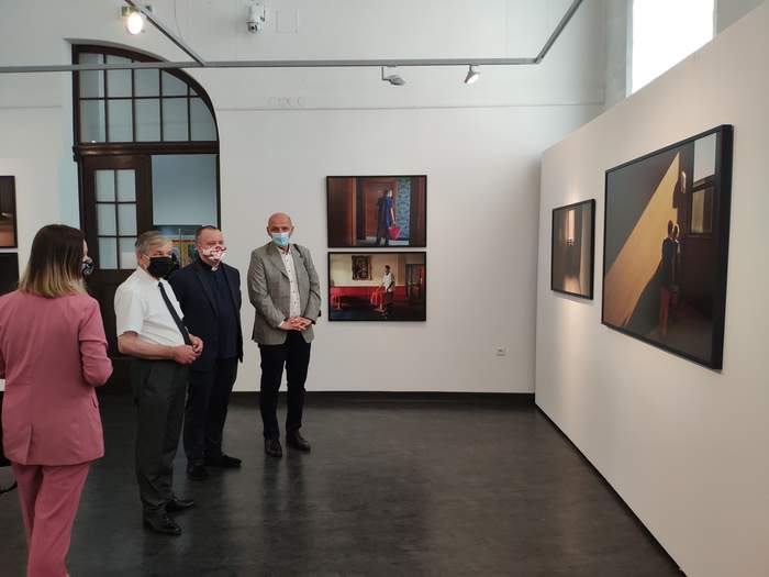 Pokaż zdjęcie: Na zdjęciu cztery osoby osoby oglądają fotografie zawieszone na białej ścianie