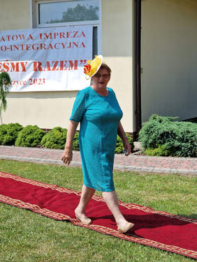 kobieta w niebieskiej sukience i żółtym kapelusiku idzie po czerwonym dywanie