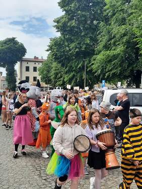 Pokaż zdjęcie: Tłum ludzi, który kroczy ulicami Wieruszowa. Wszyscy są ubrani na kolorowo i tworzą różnobarwny pochód. Dzieci są poprzebierane za różne zwierzęta. 