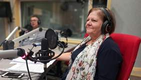 Kobieta w czarnej sukience, z kolorowym szalem na szyi, w słuchawkach na uszach