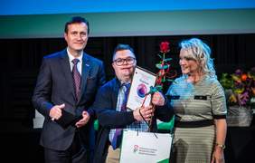 Pokaż zdjęcie: Osoba z niepełnosprawnością stoi z nagrodą na scenie, a obok Wicewojewoda Lubuski Tomasz Nesterowicz i Dyrektor Oddziału Lubuskiego PFRON Elżbieta Miernik-Krukurka