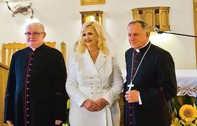 Pokaż zdjęcie: Pomiędzy księżmi stoi kobieta blondynka ubrana na biało
