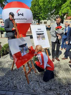 Pokaż zdjęcie: W Alei Olimpijczyków i Paraolimpijczyków w Wieruszowie paraolimpijka Ewa Zielińska podpisuje swoje zdjęcie. W dłoni trzyma czerwoną różę. Obok niej stoją mężczyźni. 
