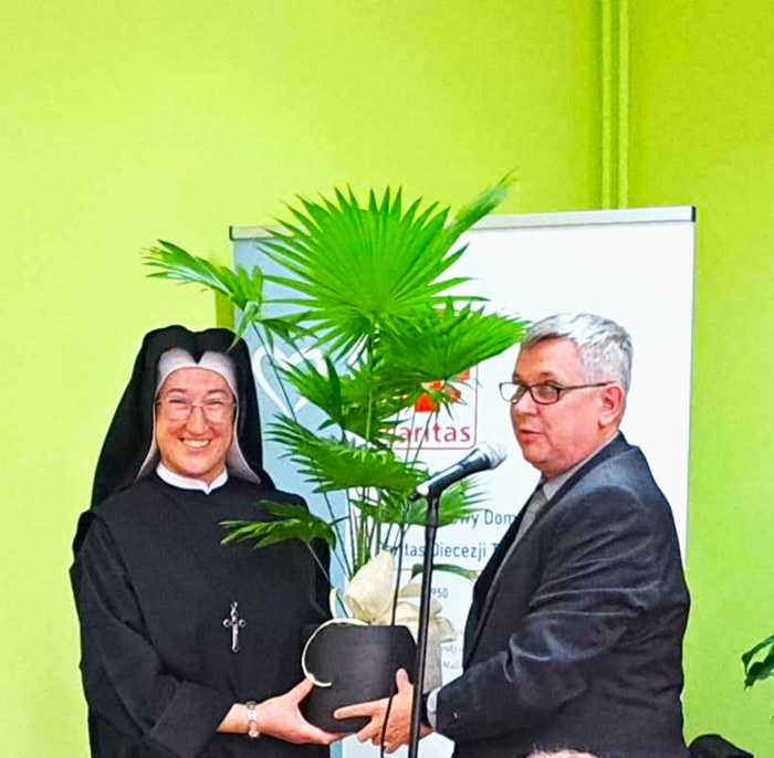 Kierowniczka ŚDS siostra Agnieszka odbiera życzenia i prezent - palmę doniczkową - od przedstawiciela PFRON - Piotra Kopycińskiego