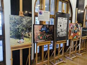 Pokaż zdjęcie: W korytarzu biblioteki na sztalugach wyeksponowano prace plastyczne, obrazy.