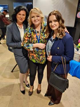 Trzy kobiety pozują do zdjęcia. Są elegancko ubrane i radosne.