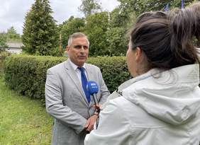 Pokaż zdjęcie: Ubrany w szary garnitur, białą koszulę i niebieski krawat mężczyzna stoi przed kobietą trzymającą mikrofon z napisem TVP3