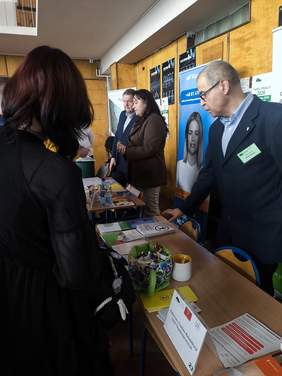 Pokaż zdjęcie: Osoba odwiedzająca rozmawia z przedstawicielem Oddziału Lubelskiego PFRON przy stoisku informacyjnym podczas Targów Pracy. 