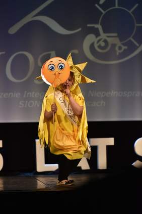 Pokaż zdjęcie: Na scenie występuje osoba w złotym stroju przebrana za słoneczko