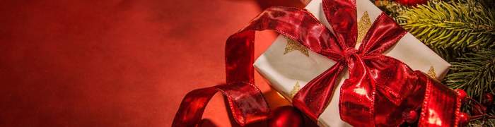 Pokaż zdjęcie: Prezent w opakowany w złoty świecący prezent zawinięty w czerwoną kokardę, Obok gałązka choinki.