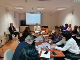 Pokaż zdjęcie: sala konferencyjna w której siedzą przy stole osoby zapisują informacje, w tle pracownik Oddziału przedstawia prezentację nowego programu Pomoc obywatelom Ukrainy z niepełnosprawnością 