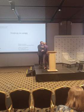 Pokaż zdjęcie: Mężczyzna w garniturze podaje rękę kobiecie, dziękuje jej za wykład. W tle na ścianie slajd z prezentacji z podziękowaniami za uwagę