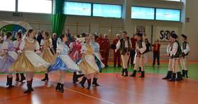 Pokaż zdjęcie: (Kilkanaście kobiet i mężczyzn w kolorowych strojach tańczy na hali