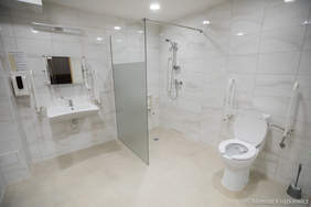 Pokaż zdjęcie: Wyremontowana nowa, biała łazienka, w pełni przystosowana do potrzeb osób z niepełnosprawnościami. Od lewej: umywalka, prysznic, muszla klozatowa.