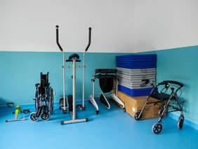 Pokaż zdjęcie: Sala ze sprzętem rehabilitacyjnym w nowym Ośrodku. Sprzęt rehabilitacyjny na tle niebieskiej ściany