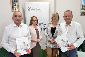 Pokaż zdjęcie: Dwie kobiety i dwóch mężczyzn - przedstawicielki Oddziału Małopolskiego PFRON oraz przedstawiciele Powiatu Dąbrowskiego stoją na tle rollupu PFRON
