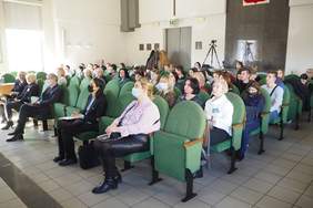 Pokaż zdjęcie: Fragment sali. W rzędach na zielonych fotelach siedzi około 50 osób w różnym wieku.