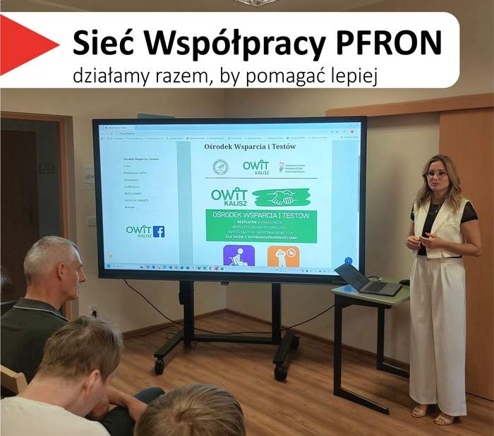 Pokaż zdjęcie: Sala szkoleniowa z uczestnikami siedzącymi tyłem do aparatu przed dużym ekranem na stojaku. Nad ekranem wisi baner z logo „Sieć Współpracy PFRON” i hasłem „działamy razem, by pomagać lepiej”. Na ekranie wyświetlana jest prezentacja z napisem „OWiT Kalisz Ośrodek Wsparcia I Testów” oraz grafiką złączonych dłoni. Po prawej stronie ekranu stoi kobieta, która prowadzi spotkanie. Obok niej na małym stoliku, znajduje się otwarty laptop.