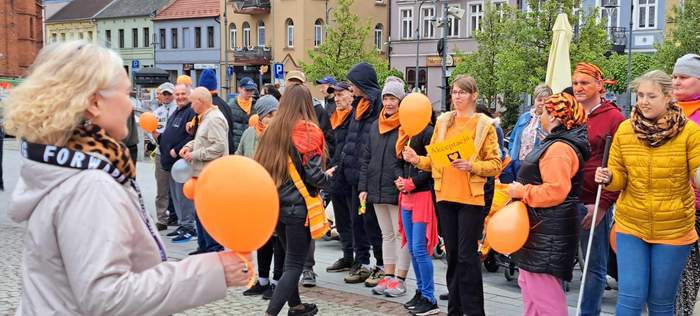 Uczestnicy marszu tańcza na rynku w Wąbrzeźnie, trzymając w dłoniach pomarańczowe balony