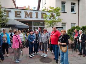 Pokaż zdjęcie: Przed budynkiem stoi duża grupa osób. Na obiekcie znajduje się napis "Temida". 