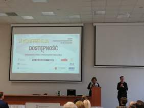 Pokaż zdjęcie: Slajd z nazwą konferencji, dwie kobiety ubrane na czarno