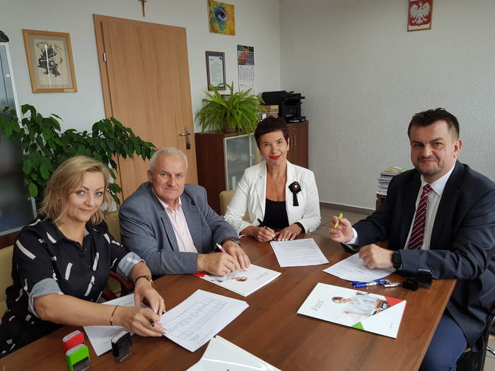 Pokaż zdjęcie: Władze Powiatu Żarskiego oraz Dyrektor Oddziału w trakcie podpisywania umów w gabinecie Dyrektora, wszyscy są uśmiechnięci i trzymają w ręku długopisy