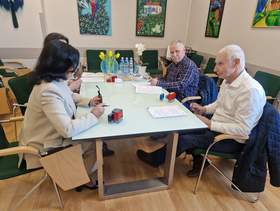 Dwie kobiety i dwóch mężczyzn siedzi przy stole w sali konferencyjnej. Na stole są rozłożone dokumenty.