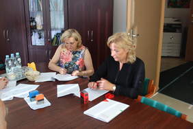Pokaż zdjęcie: Zdjęcie pokoju w biurze, przy stole siedzą dwie kobiety podpisujące dokumenty, które leżą na stole