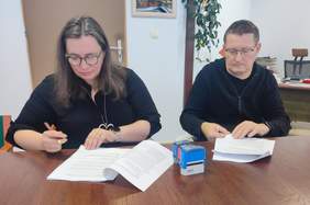 Pokaż zdjęcie: Przy stole w gabinecie kobieta i mężczyzna podpisują umowę.