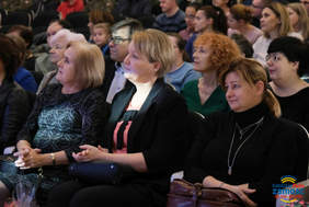 Pokaż zdjęcie: Zdjęcie widowni, w sali w fotelach siedzi publiczność, zbliżenie na trzy kobiety
