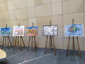 Pokaż zdjęcie: Na tle kamiennej ściany stoją sztalugi, a na nich jest wyeksponowanych pięć obrazów