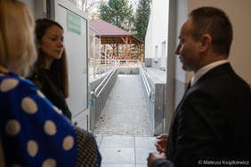 Pokaż zdjęcie: Przez otwarte drzwi budynku goście oglądają podjazd dla osób na wózkach inwalidzkich