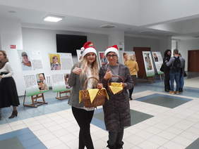 Pokaż zdjęcie: Pracownice PFRON w czapkach św. Mikołaja trzymające koszyczek ze słodyczami