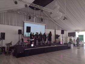 na scenie stoi 10 osób, występ, z prawej strony sceny kobieta robi zdjęcie