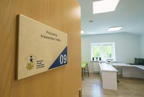 Pokaż zdjęcie: Uchylone drwi do sali. Na drzwiach tabliczka z napisem "Pracownia krawiectwa i haftu"