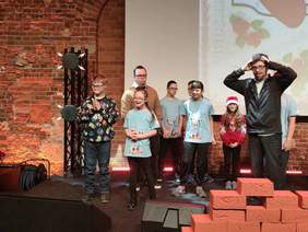 Pokaż zdjęcie: Na scenie stoją dzieci z Zespołem Downa. Uśmiechają się. Są kolorowo ubrane. 