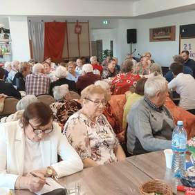 Pokaż zdjęcie: Kilkadziesiąt osób siedzi przy trzech stołach i rozmawia.