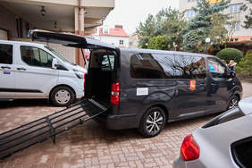 Pokaż zdjęcie: Dziewięciomiejscowy mikrobus przystosowany do przewozu osób z niepełnosprawnościami z rozłożoną rampą wjazdową.