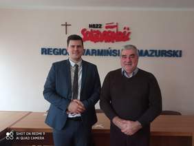 Pokaż zdjęcie: Panowie stoją na tle loga Solidarności