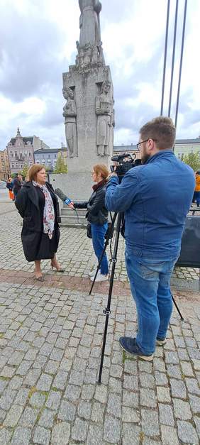 Na pierwszym planie, po prawo stoi kamerzysta ze sprzętem, a po lewej - w tle - Dyrektor Kujawsko-Pomorskiego Oddziału PFRON udziela wywiadu dla Pani redaktor z TVP Wąbrzeźno