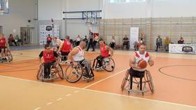 Pokaż zdjęcie: na sali sportowej osoby na wózkach inwalidzkich grają mecz koszykówki.