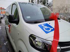 Pokaż zdjęcie: na zdjęciu biały ze znakiem przewóz dla osób niepełnosprawnych, bus ma założoną czerwoną kokardę 