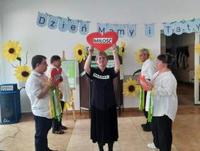 Pokaż zdjęcie: Osoby z niepełnosprawnością biorą udział w występie artystycznym. Kobieta trzyma serce z napisem "Miłość". Obok niej stoją inne osoby. 